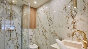 Une salle de bain moderne avec une douche à parois de verre, un pare-baignoire en marbre et un robinet doré.