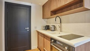 Une cuisine de taille réduite avec une porte sombre, des placards en bois, un plan de travail blanc, un évier en acier inoxydable et un four encastré.