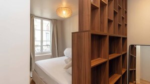 Une chambre à coucher avec un lit, une armoire en bois, une fenêtre avec des rideaux et un luminaire au plafond.