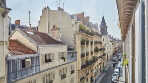 Une rue étroite bordée d’immeubles à plusieurs étages, avec des balcons et un clocher d’église imposant.