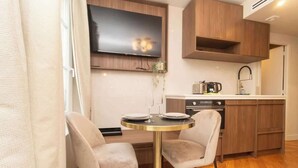 Une cuisine moderne avec des meubles en bois, un téléviseur à écran plat, une table à manger avec deux chaises et une machine à café.