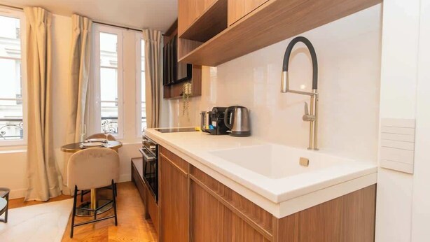 Une cuisine de taille réduite avec un plan de travail blanc, un robinet noir et des armoires en bois.