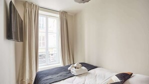 A bedroom with a bed, a TV mounted on the wall, and a window with curtains.