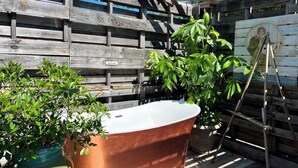 Eine rustikale Outdoor-Umgebung mit Holzzaun, Kupferbadewanne und Pflanzgefäßen.