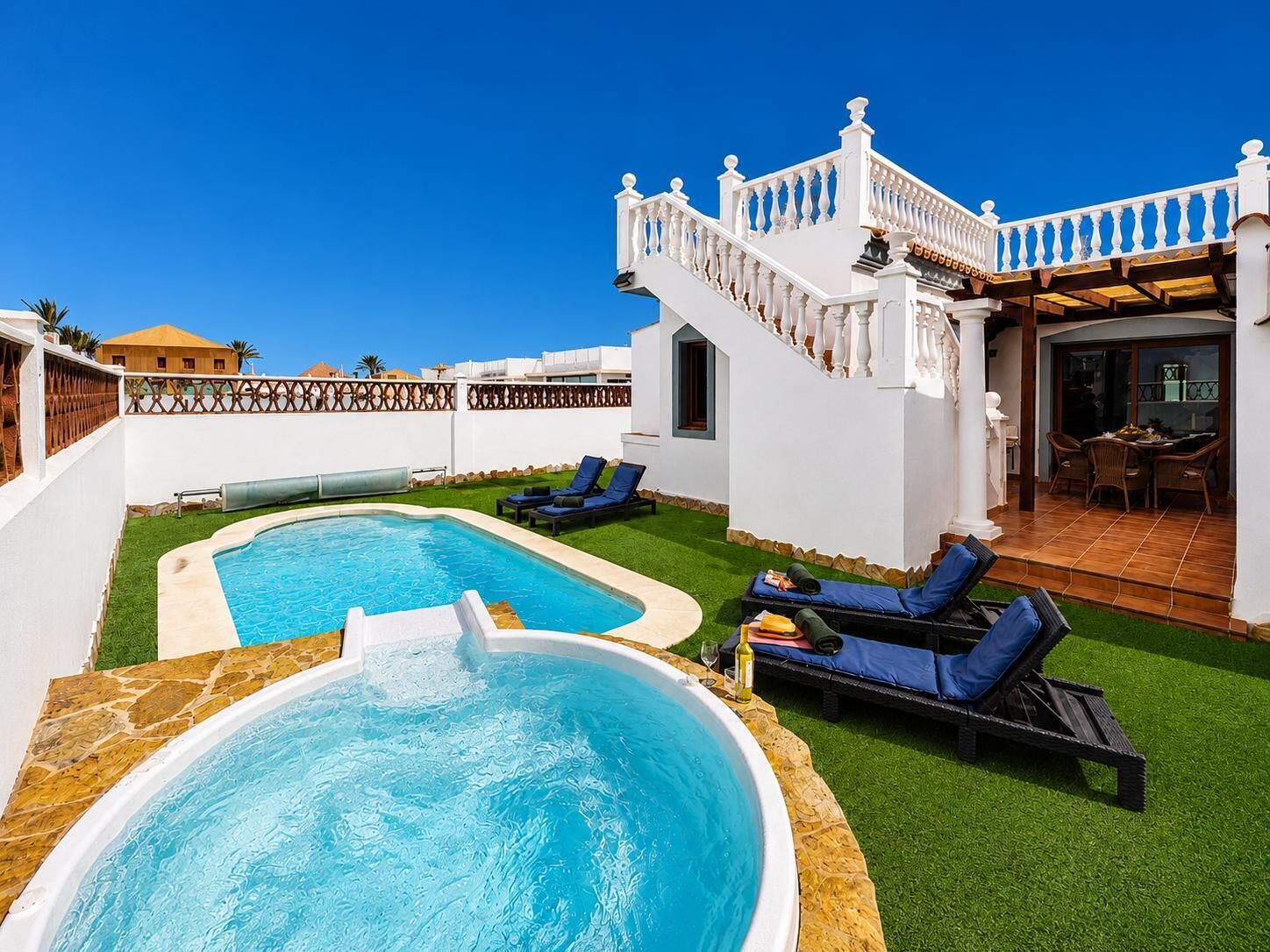 Zona de piscina amb banyera d'hidromassatge, gandules i una escala que condueix a un porxo cobert.
