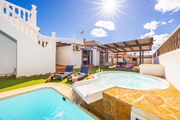 Ein Poolbereich mit Whirlpool, Liegestühlen und einer Pergola.
