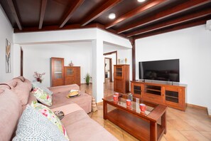 A living room with a sofa, a coffee table, and a TV. There are wooden cabinets and a plant.