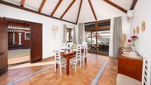 Un comedor con mesa y sillas de madera, vistas al exterior por una puerta de cristal y un jarrón decorativo sobre una mesita auxiliar.