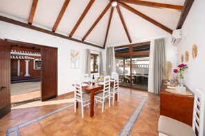 A dining area with a wooden table and chairs, a view through a glass door to an outdoor space, and a decorative vase on a side table. - Villa Thomas - Four Bedroom Villa, Sleeps 8 (Corralejo)