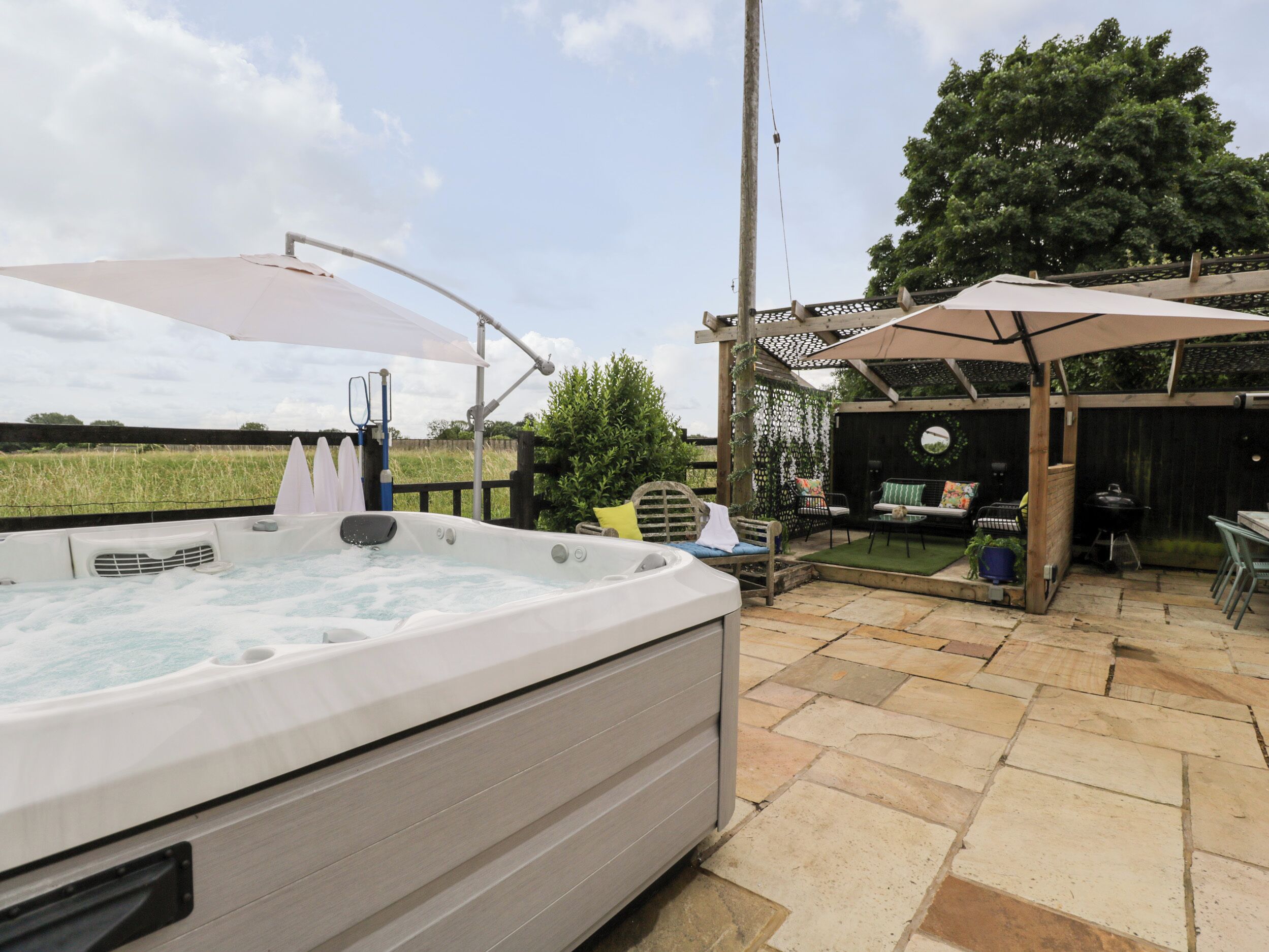 Un jacuzzi en un patio trasero con una pérgola, asientos exteriores y una parrilla.