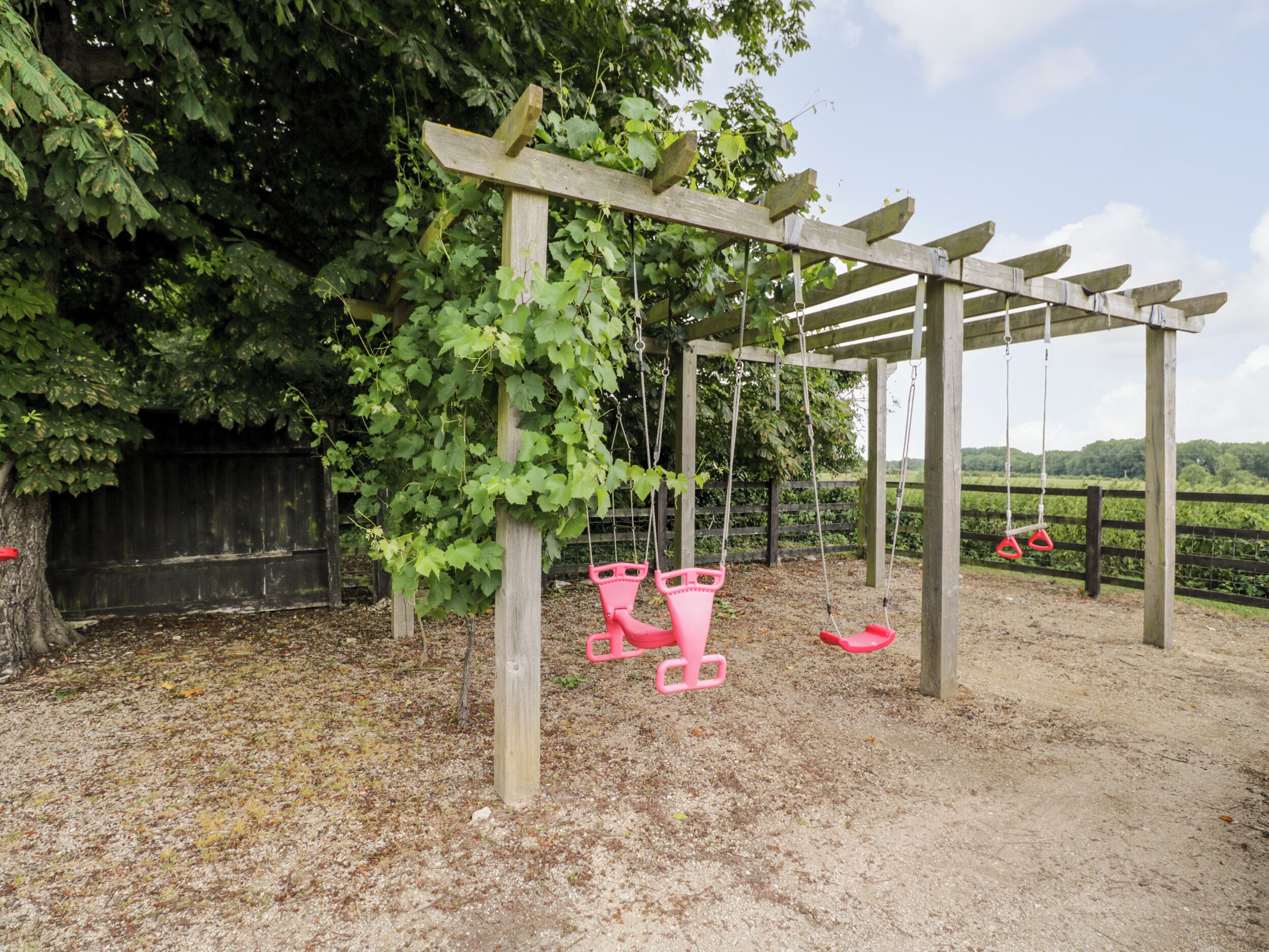 Eine Holzschaukel mit zwei rosafarbenen Sitzen und einer hölzernen Pergola.