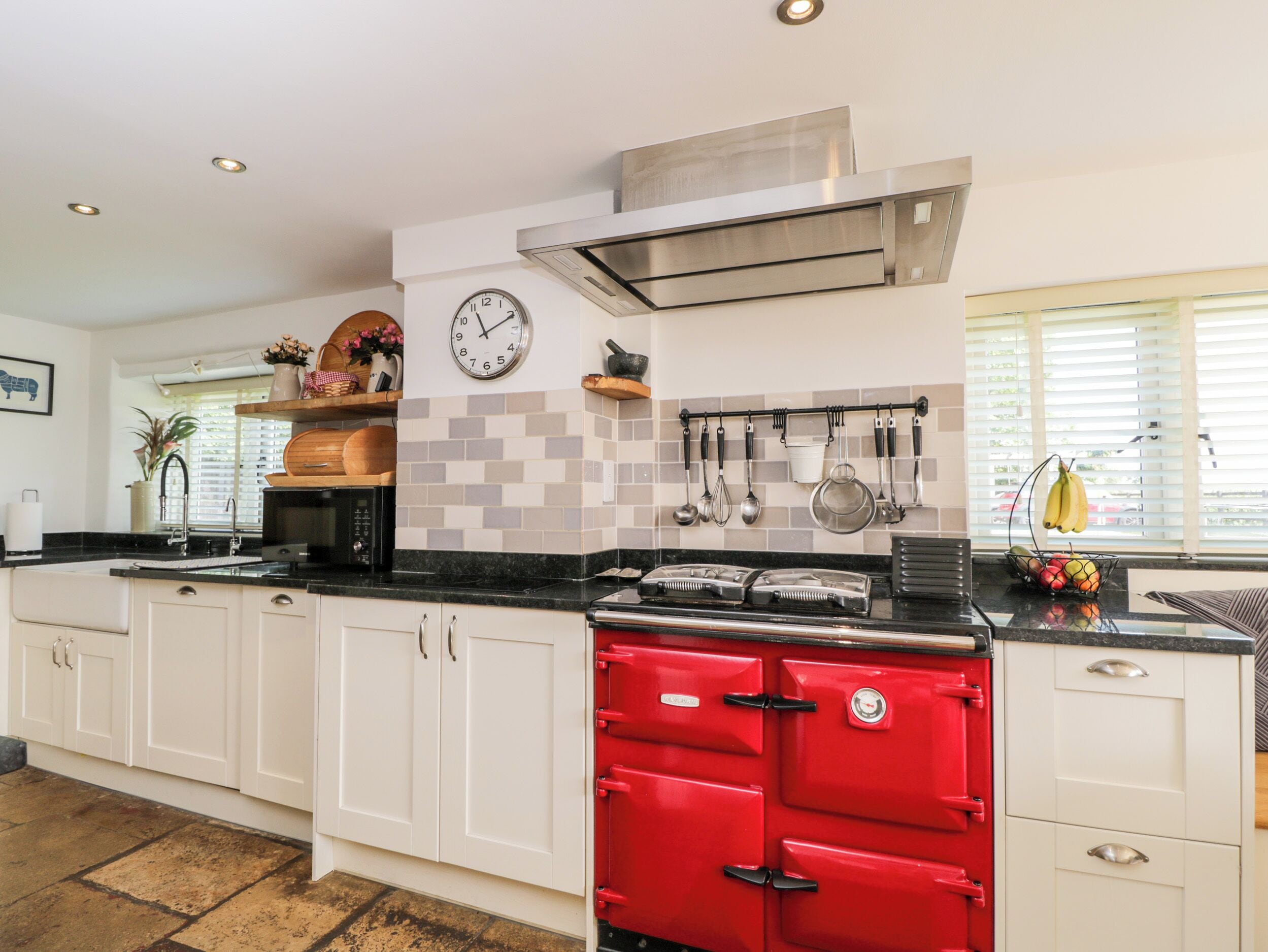 Una cocina con gabinetes blancos, una estufa roja, un reloj y varios utensilios de cocina colgados en la pared.
