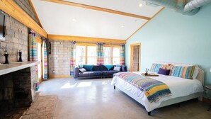 Quarto com cama grande, sofá, lareira e janela com cortinas.