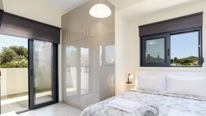 Ein modernes Schlafzimmer mit einem großen Bett, einer Schiebetür zum Balkon und Blick ins Grüne.