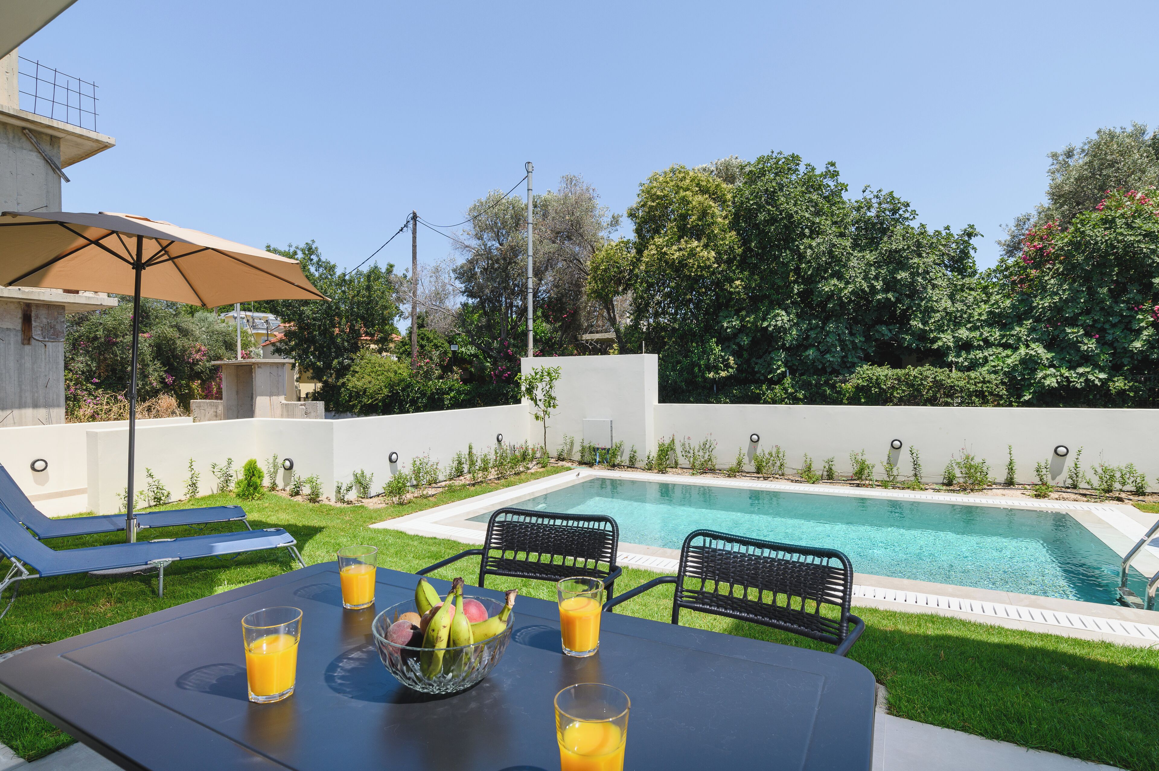 Zona junto a la piscina con una mesa, sillas y un frutero.