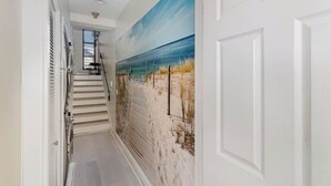 Un couloir avec un escalier menant à un palier, une porte blanche et une fresque murale sur le thème de la plage.