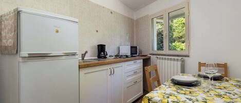 A kitchen with a refrigerator, microwave, coffee maker, and a dining table with a lemon-patterned tablecloth.