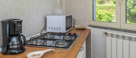 A kitchen with a gas stove, a coffee maker, a microwave, and a window with a view of greenery.