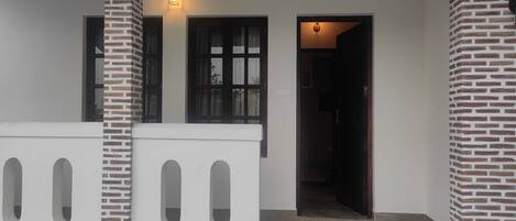 Un edificio con fachada blanca, columnas de ladrillo y una zona de entrada con baldosas.
