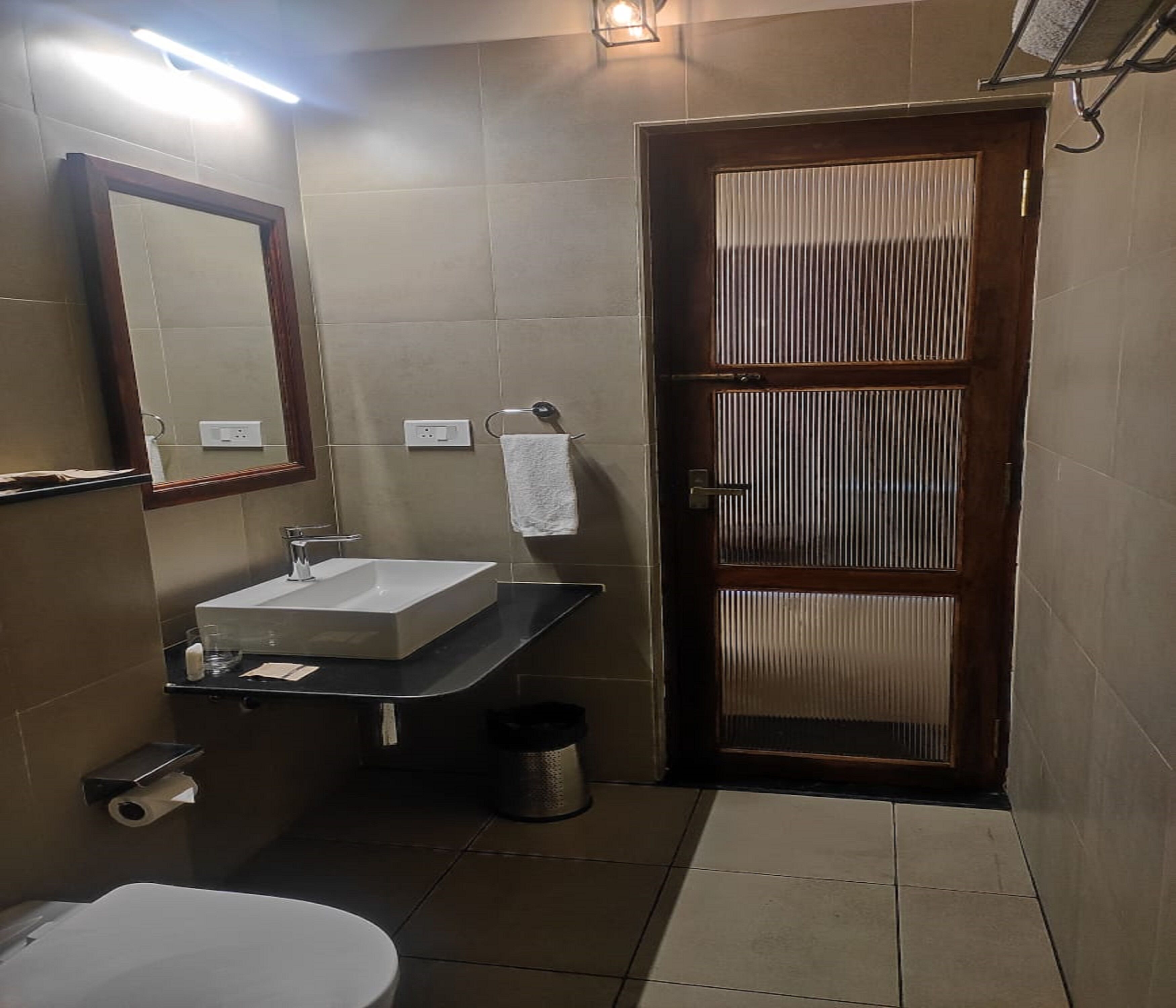 Casa de banho com lavatório, espelho, sanita e porta com janela.