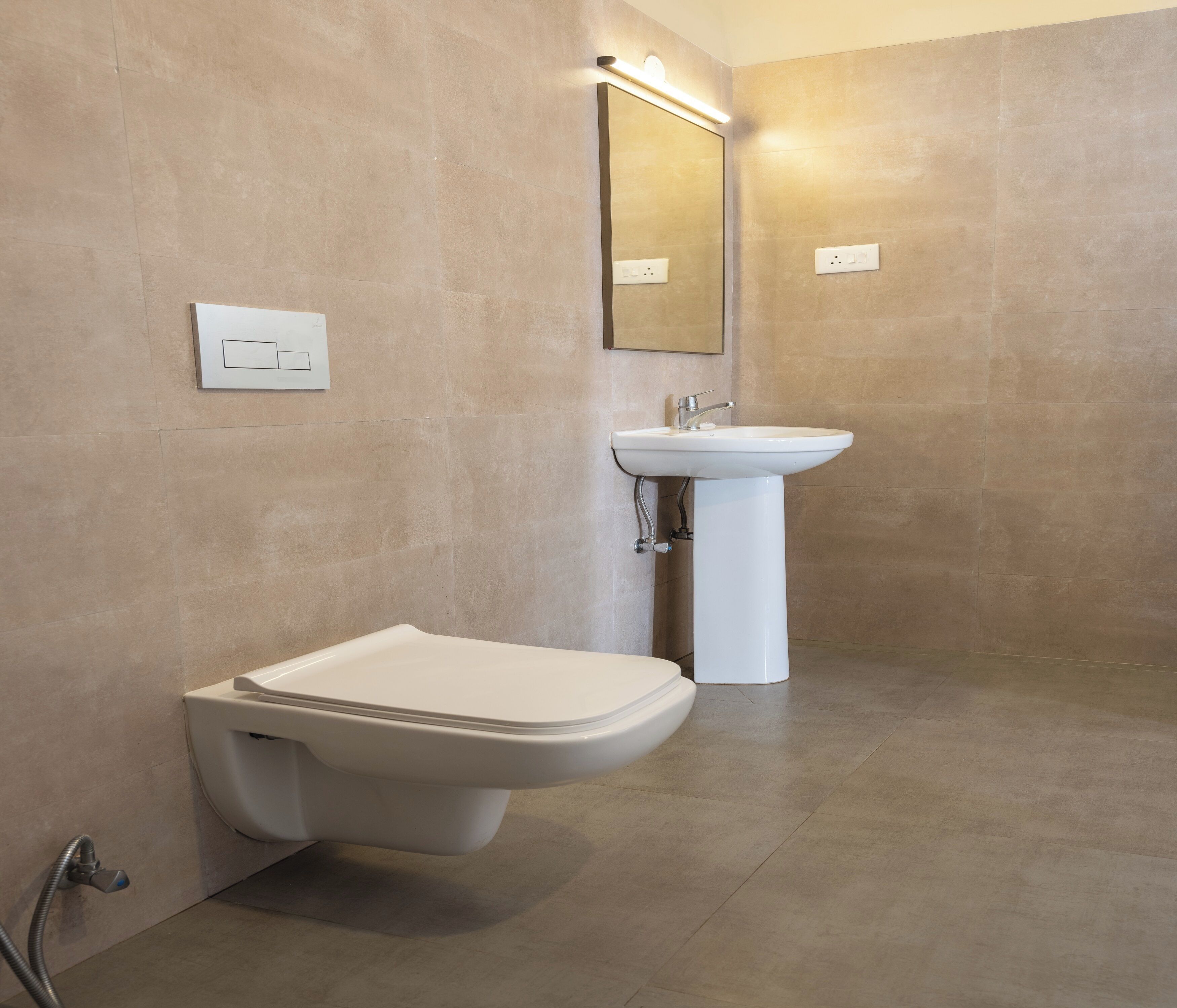 Ein modernes Badezimmer mit Wand-WC, Waschbecken auf Säule und großem Spiegel.
