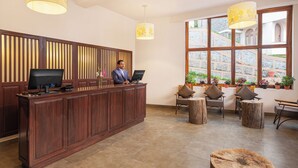 A reception desk with a computer, a man standing behind it, and a seating area with chairs and a round wooden table. - Mango Hill Kodai (Kodaikanal)