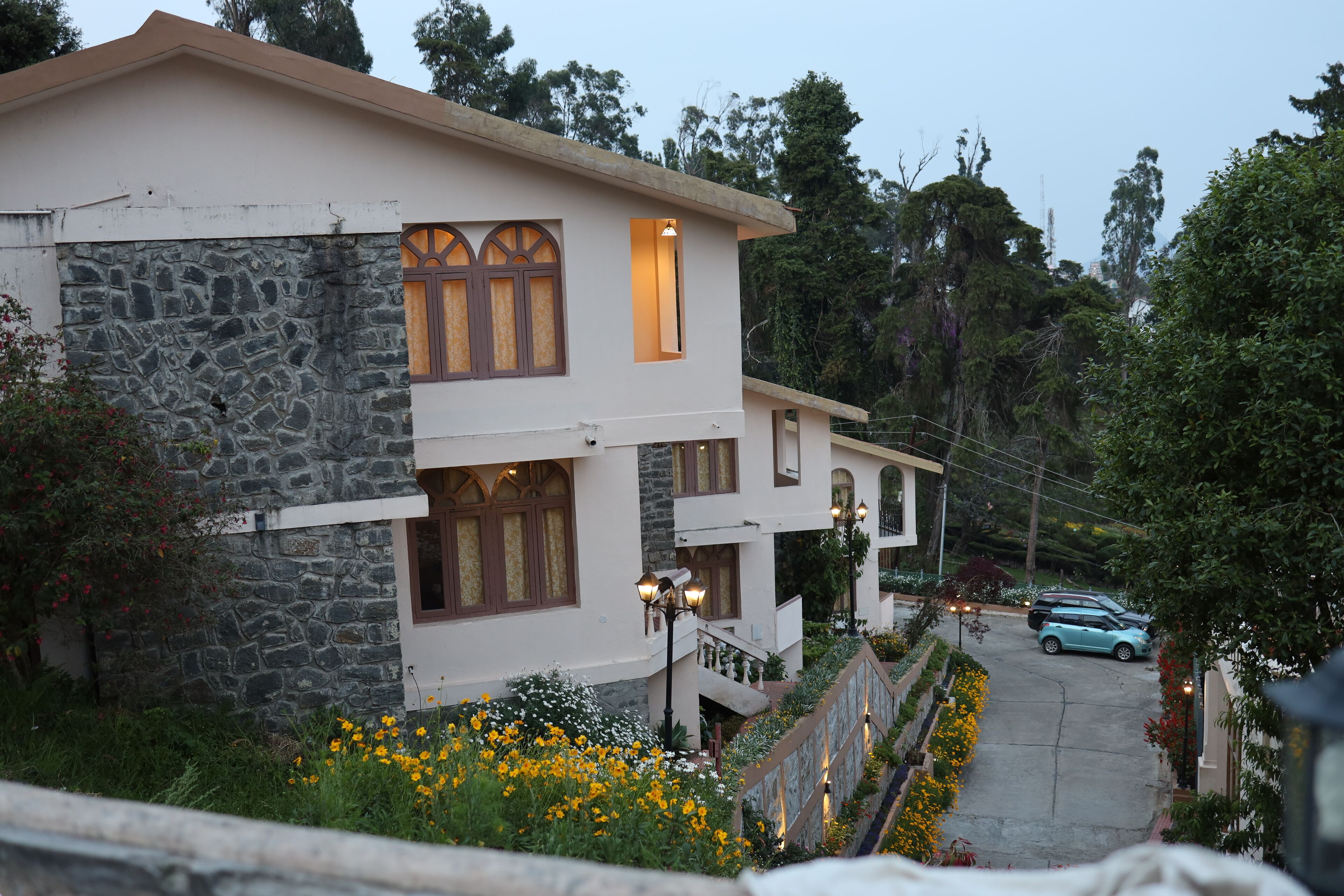 A multi-story building with stone and plaster walls, a balcony, and a flower garden.