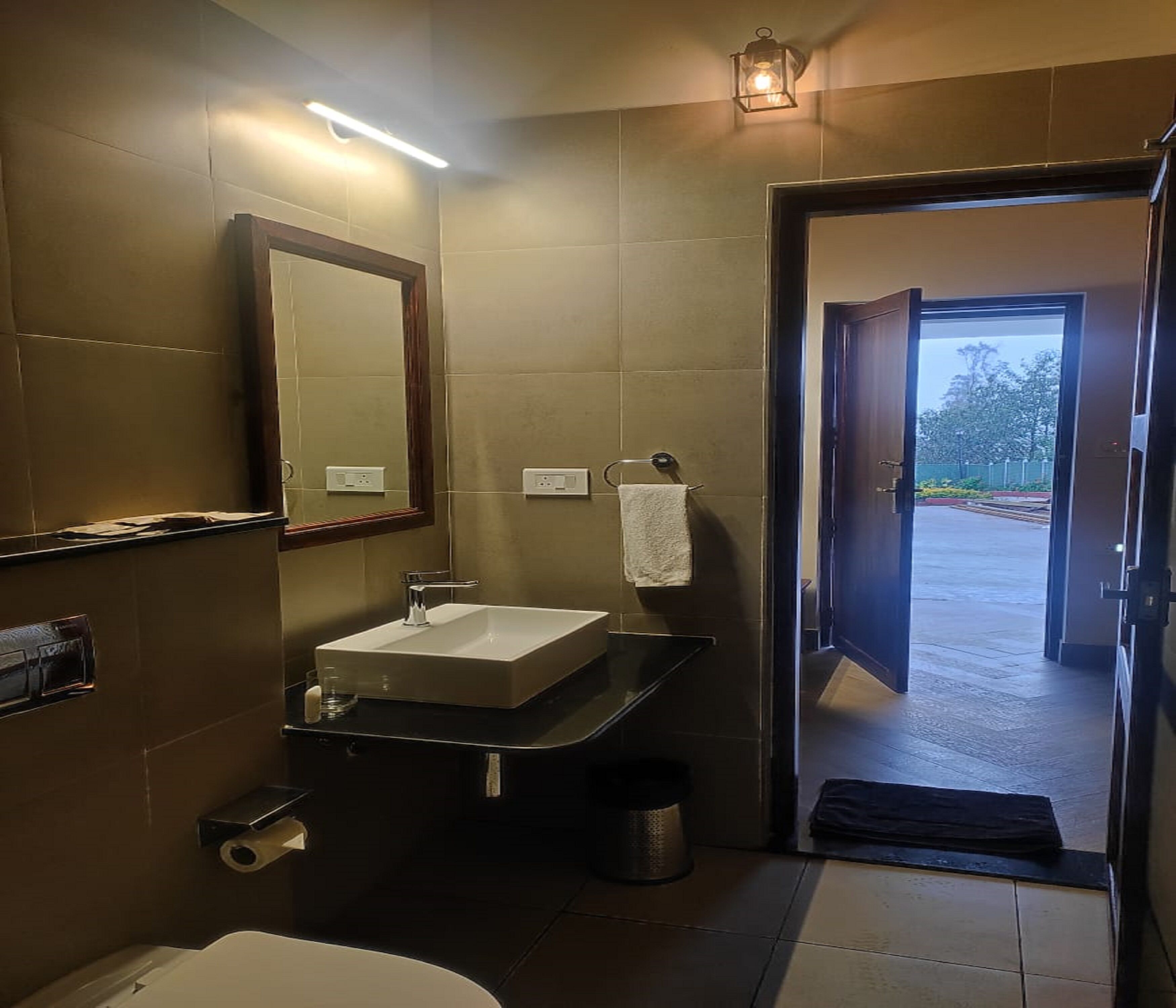 A modern bathroom with a large mirror, a sink, and a toilet. There is a towel hanging on the wall and a trash can near the sink.