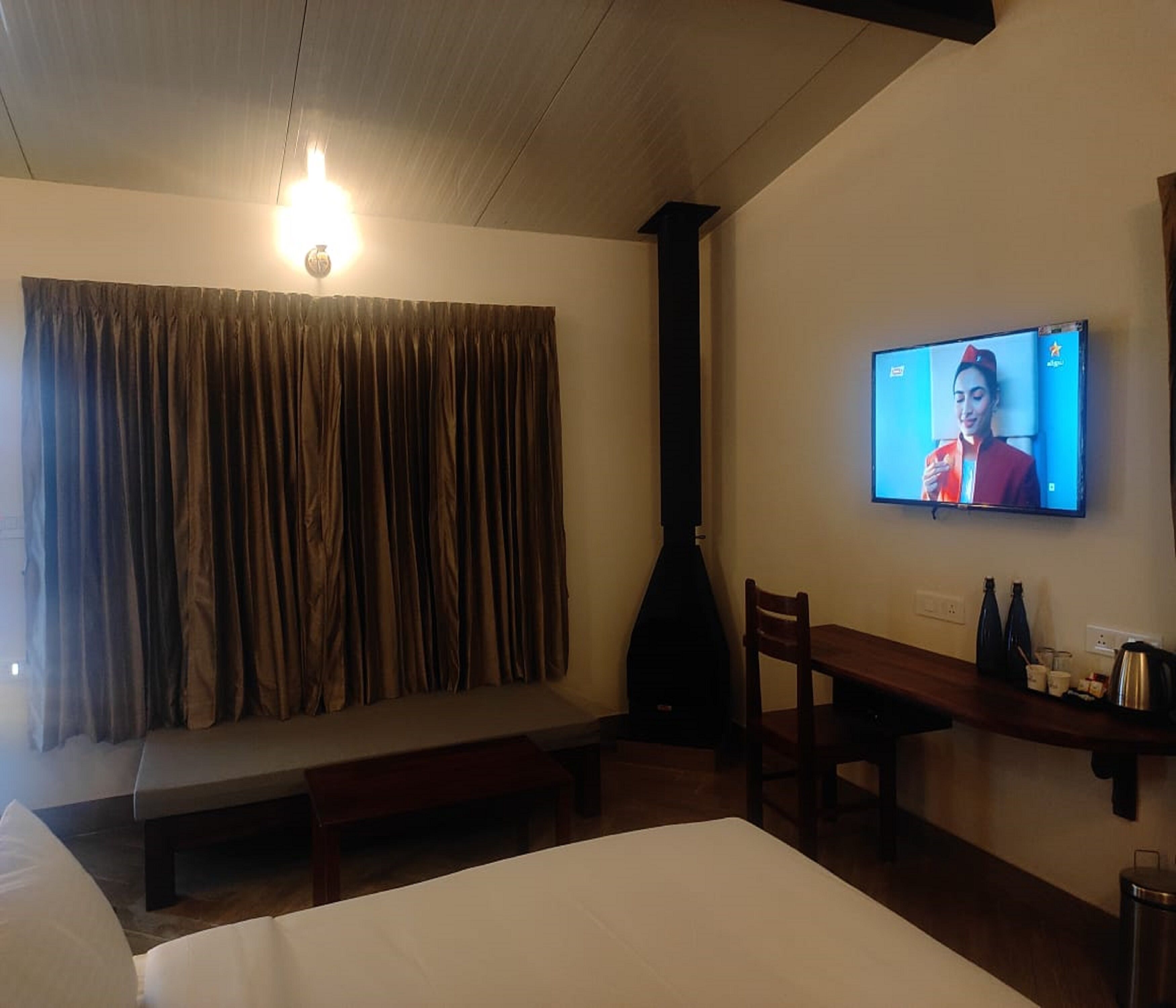 Habitación de hotel con cama, escritorio, silla, televisión y ventana con cortinas.