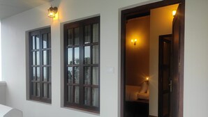 A hallway with two windows, a door leading to a room, and a wall-mounted light fixture. - Mango Hill Kodai (Kodaikanal)