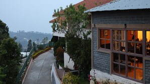 A two-story building with a red-tiled roof, large windows, and a view of a hilly landscape. - Mango Hill Kodai (Kodaikanal)