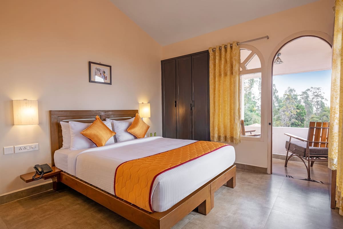 Habitación de hotel con una cama grande, dos lámparas de noche, un teléfono y vistas al exterior a través de un ventanal arqueado.