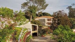 A hillside villa with a stone facade, a covered patio, and a driveway leading to a gated entrance. - Mango Hill Kodai (Kodaikanal)