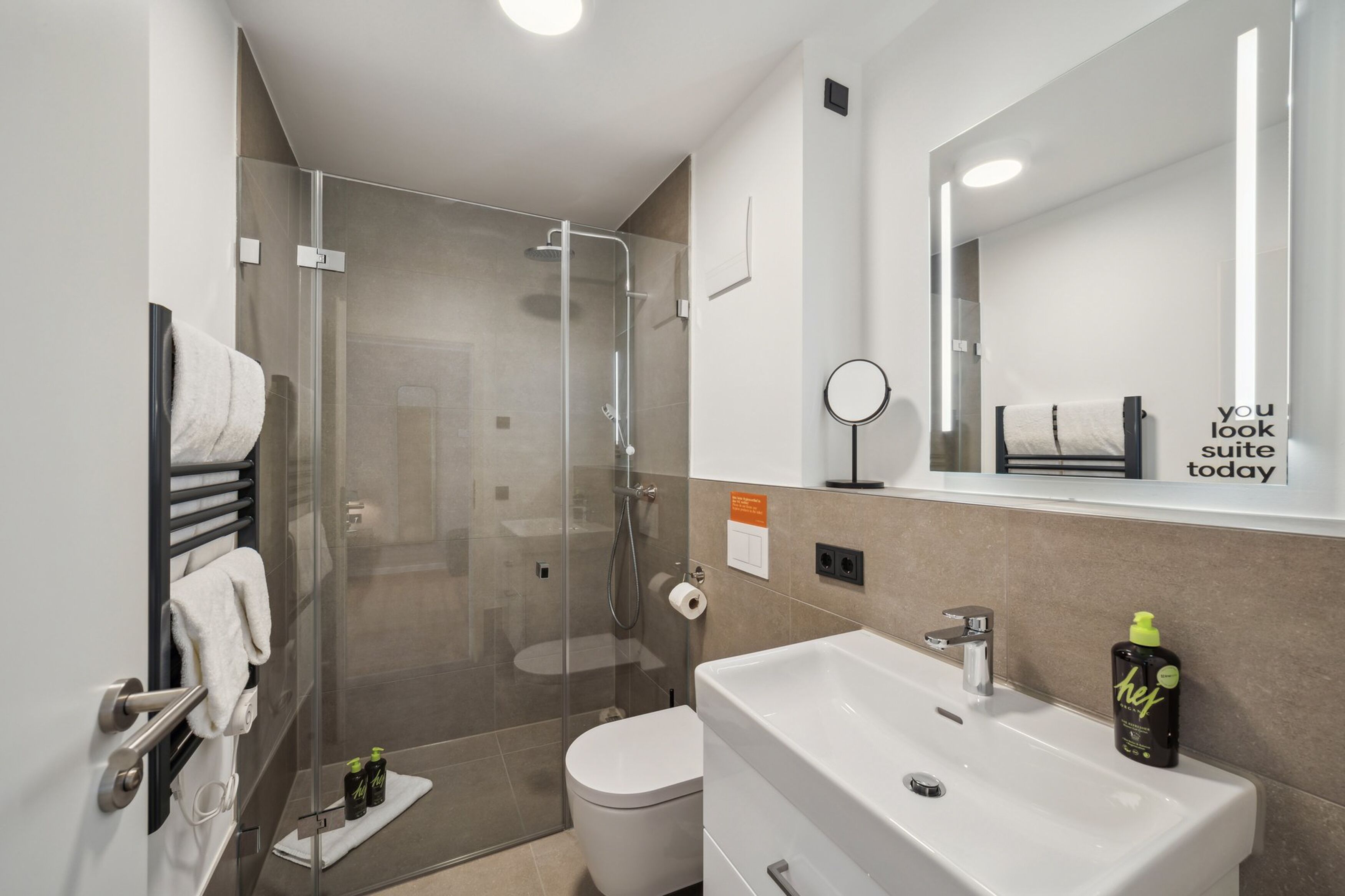 Een moderne badkamer met een douche in een glazen cabine, een witte wastafel en een spiegel met een motiverende quote.