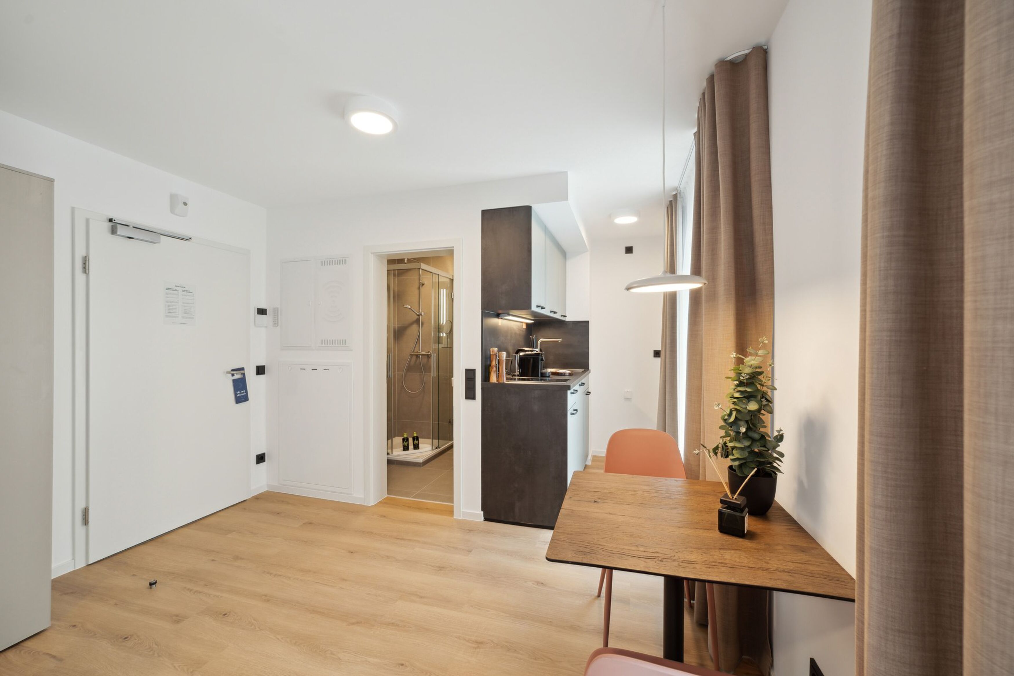 A modern kitchen with a dark countertop, a wooden dining table, and a potted plant.