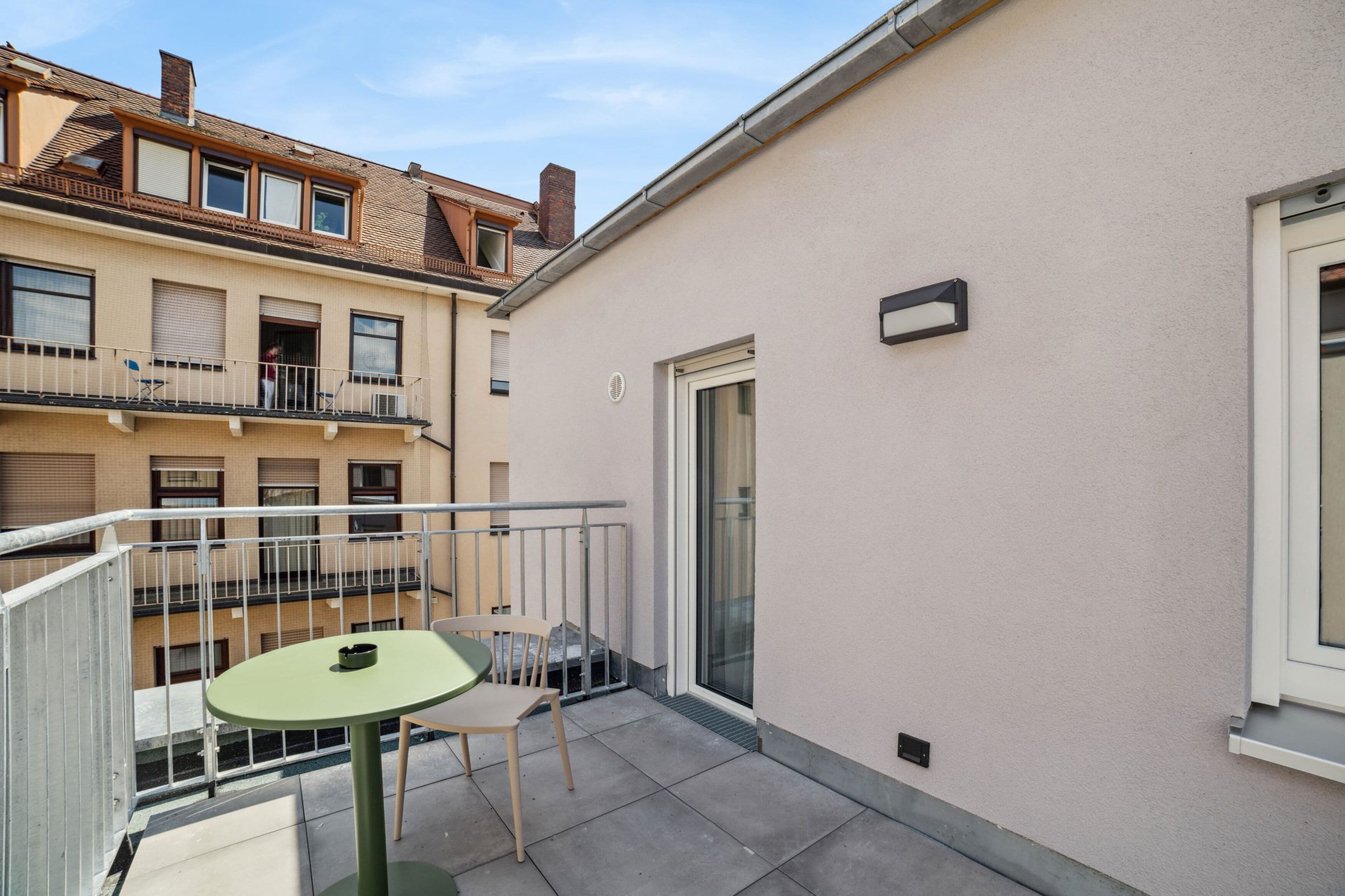 Ein kleiner Balkon mit Tisch und Stühlen, eine Schiebetür und Blick auf umliegende Gebäude.