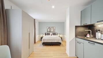 Un dormitorio moderno con una cama grande, mesitas de noche y una pequeña kitchenette con lavamanos y armarios.