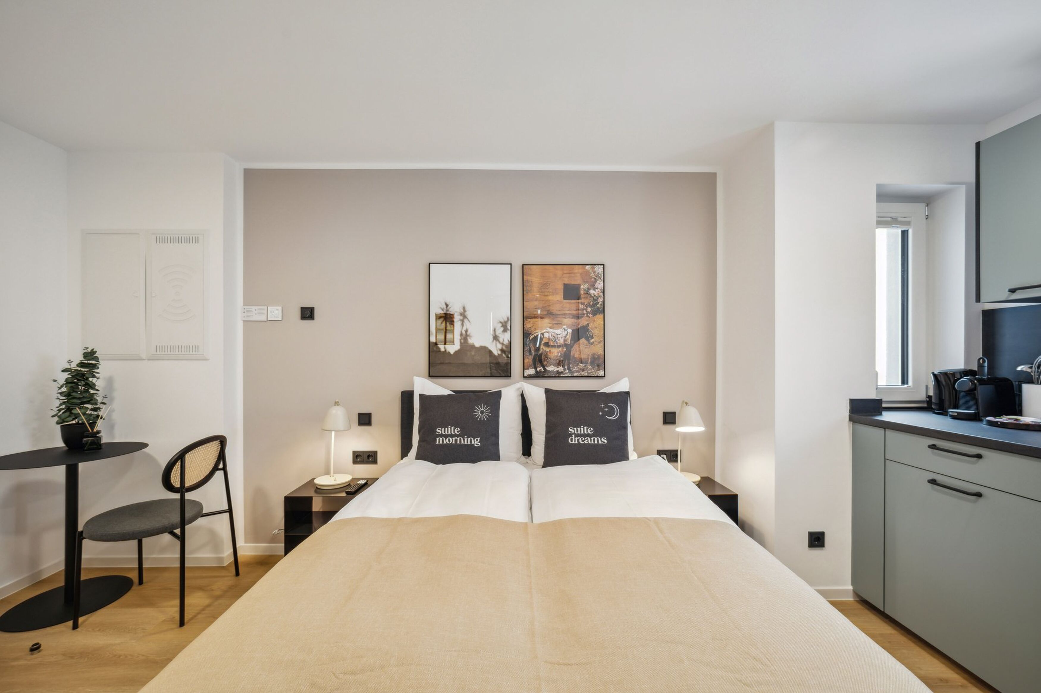 Habitación de hotel moderna con una cama grande, una pequeña mesa con una silla, un escritorio y una kitchenette.