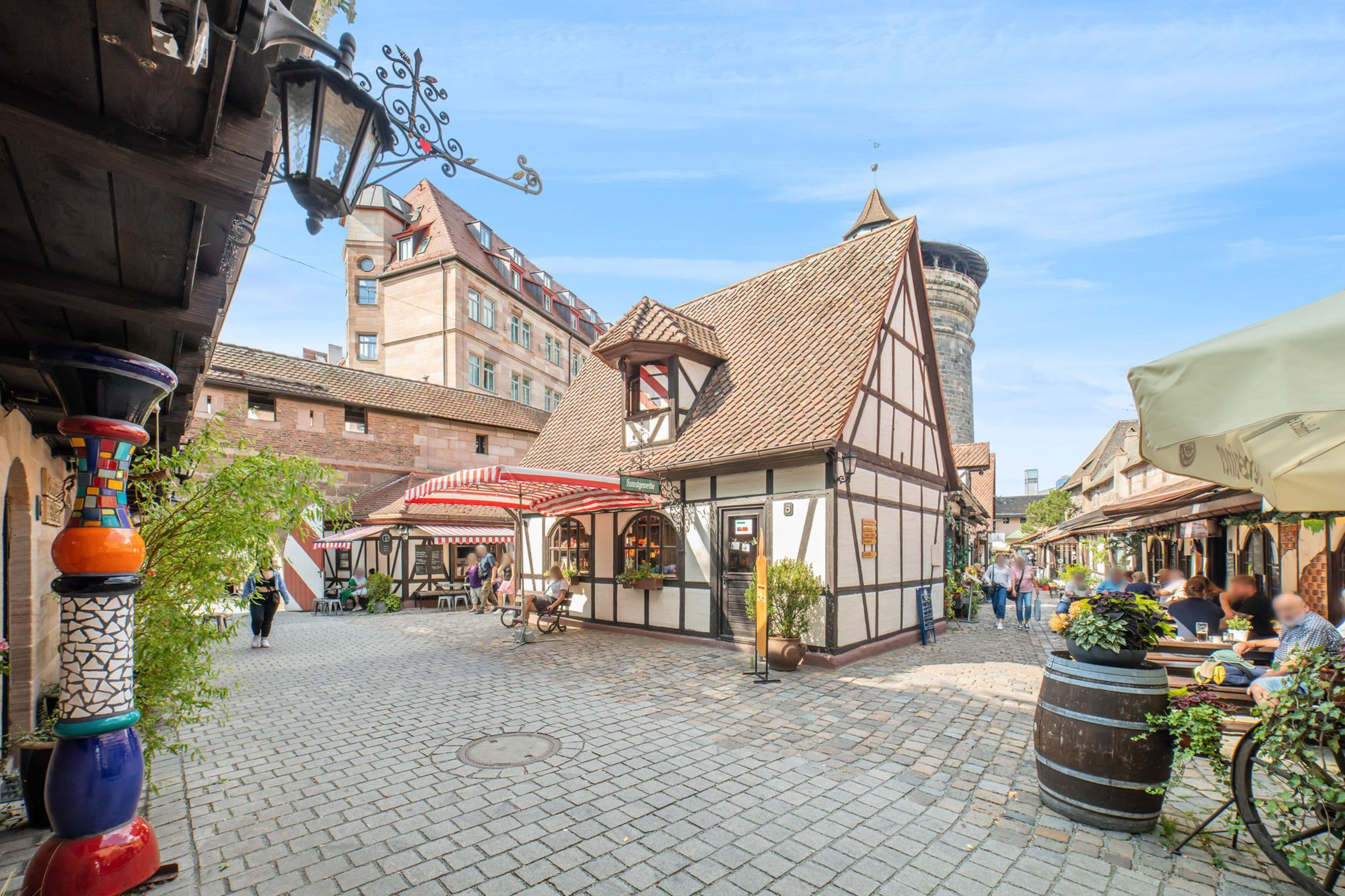 Eine Kopfsteinpflasterstraße gesäumt von traditionellen Fachwerkhäusern, mit Außenbereichen zum Sitzen und einem strahlend blauen Himmel.