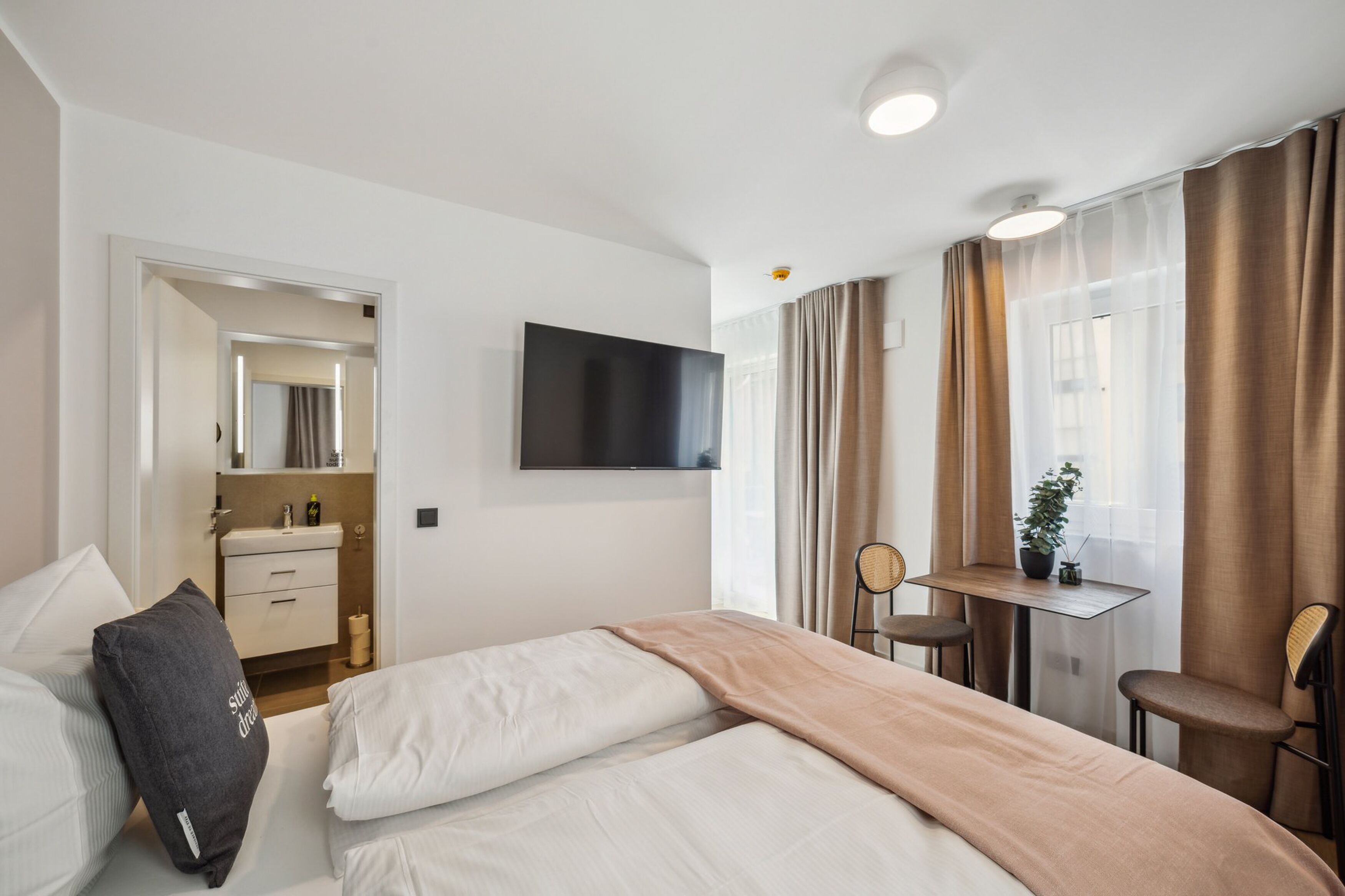 A hotel room with a bed, bedside table, TV, and a small desk with a chair.