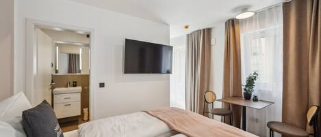 A hotel room with a bed, bedside table, TV, and a small desk with a chair.