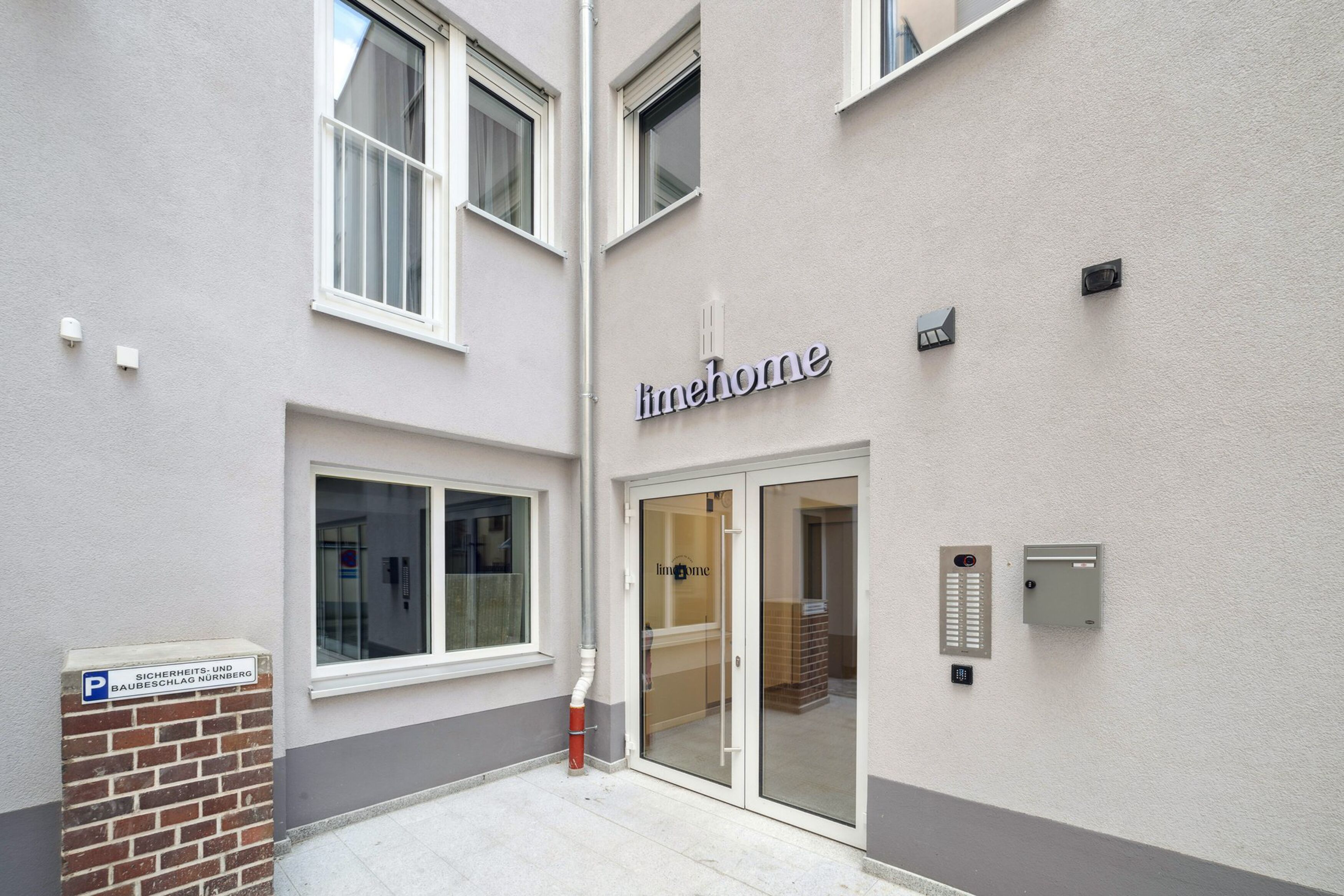 Une entrée d’immeuble avec une porte en verre, une enseigne indiquant « lmehome » et un coffre de sécurité.