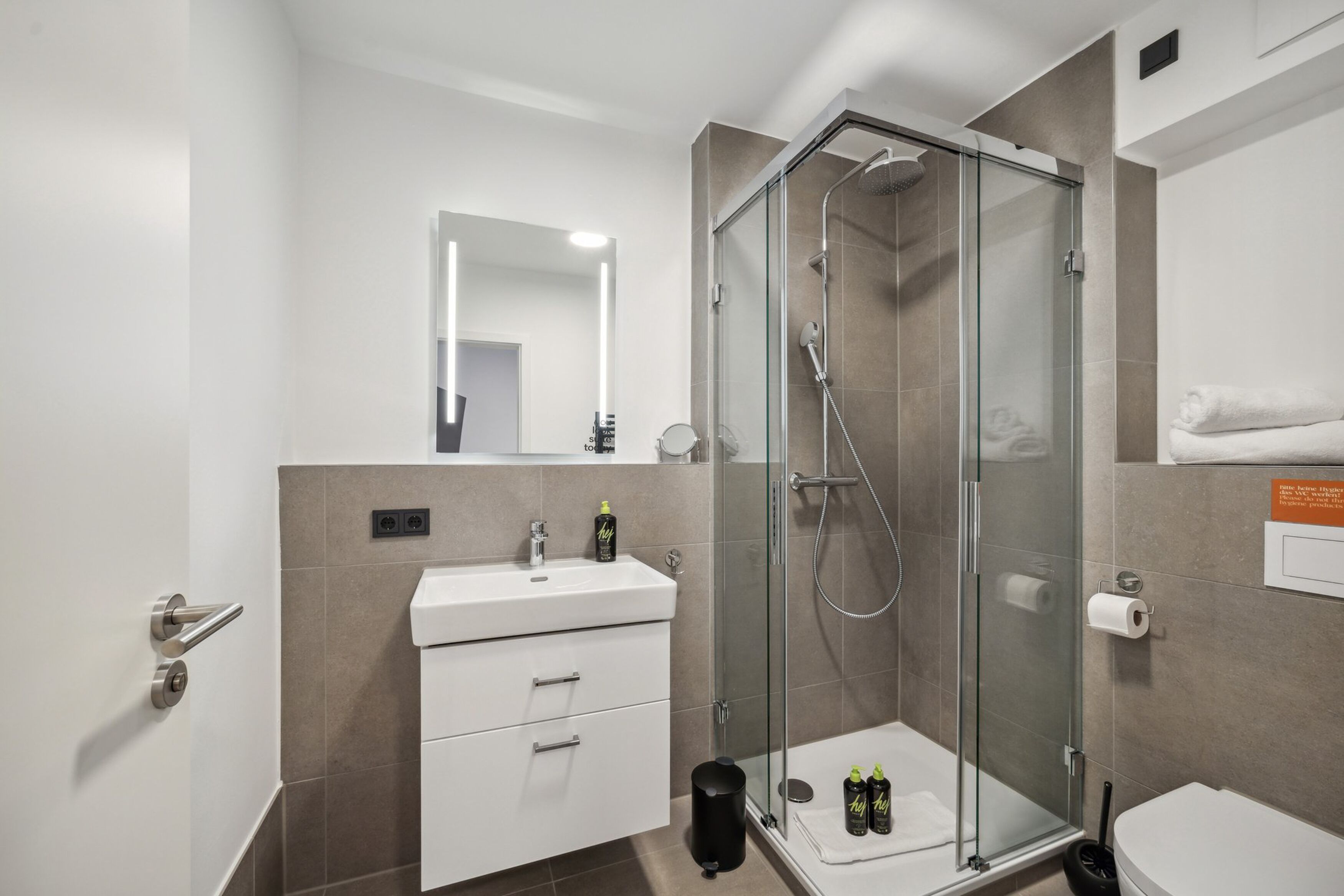 Ein modernes Badezimmer mit einer begehbaren Glasdusche, einem weißen Waschbecken und einem Spiegel darüber.