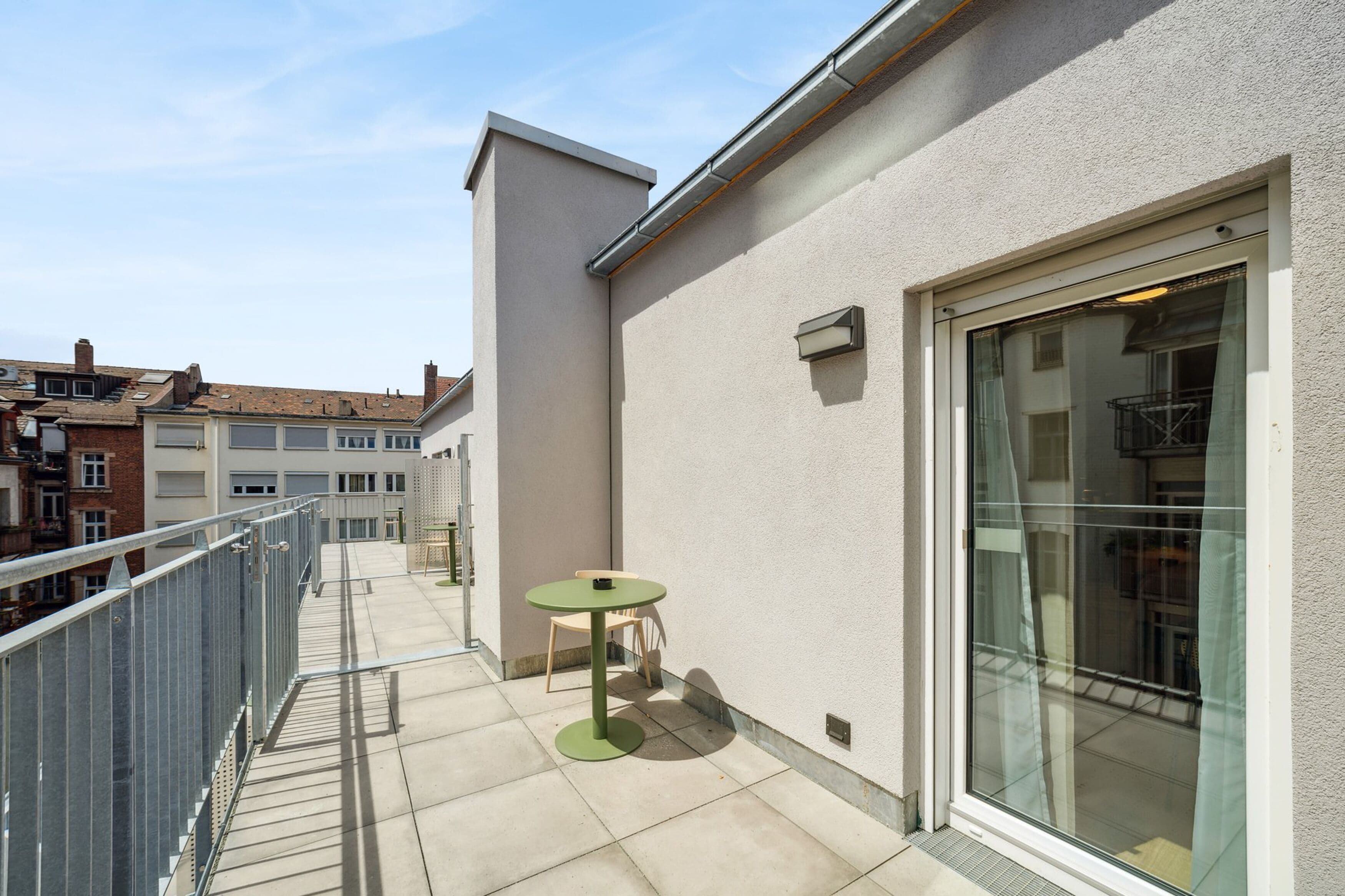 Un balcon avec une table et des chaises, une porte vitrée et une rambarde en métal.