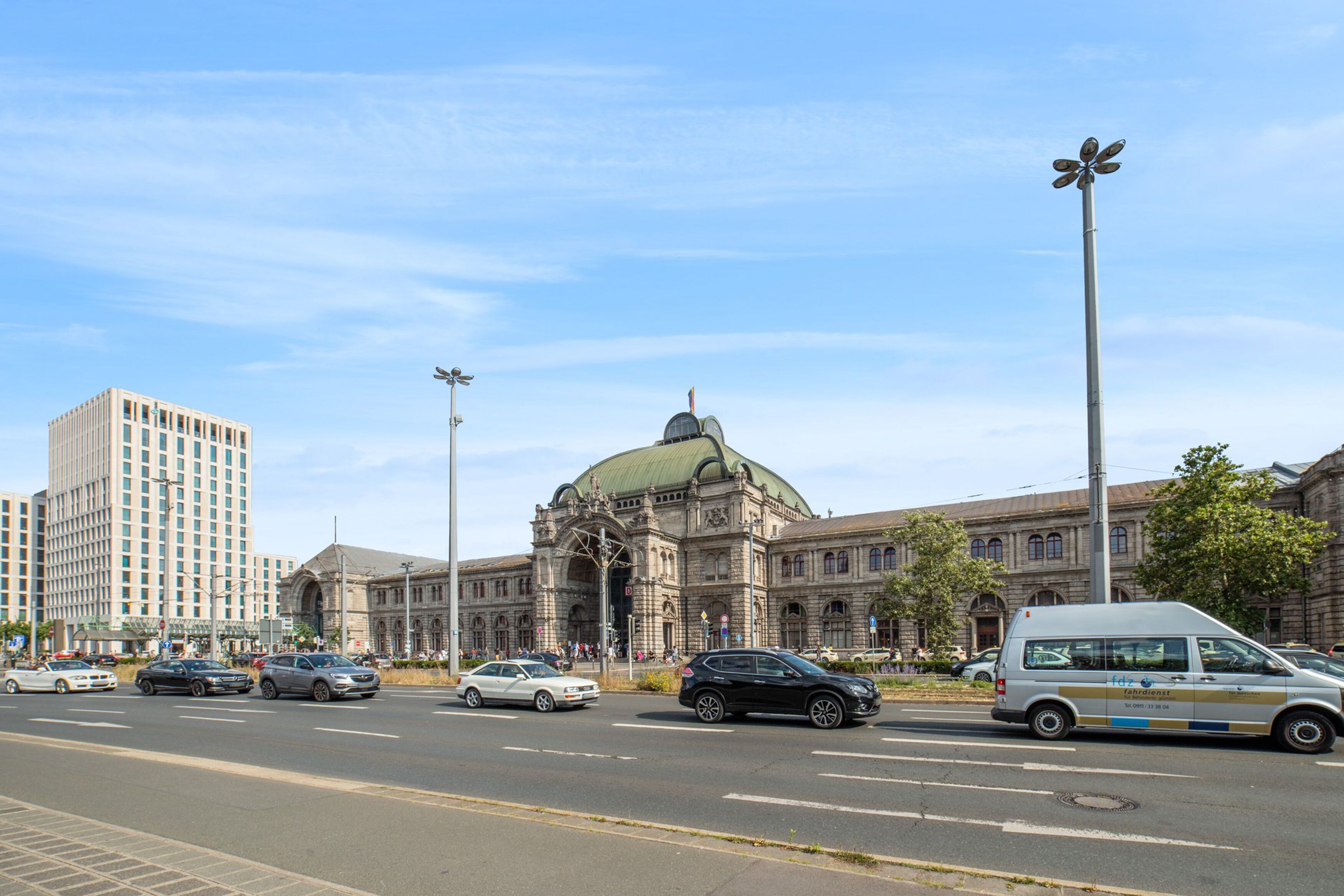 Eine Straße mit Autos und einem Lieferwagen, ein großes Gebäude mit Kuppel und eine hohe Straßenlaterne.