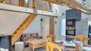 Una cocina moderna con electrodomésticos integrados, un comedor con mobiliario de madera y una escalera con vigas a la vista.