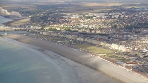 Vista aérea de una ciudad costera con una extensa playa de arena, una zona urbana densa y una mezcla de edificios residenciales y comerciales.