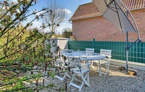 A patio with a table and chairs, a brick building in the background, and a green fence. - Clos Marie-Louise
Meublé 3 étoiles (OFFRANVILLE)