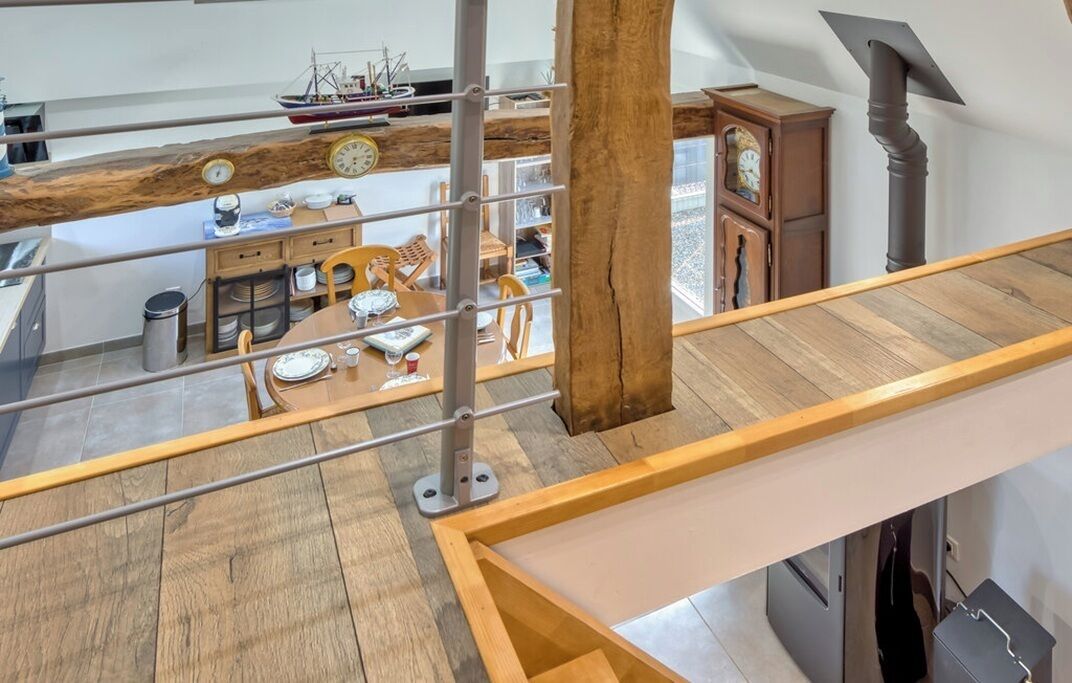 A high-ceilinged room with a wooden beam ceiling, a dining area with a table and chairs, and a large window.