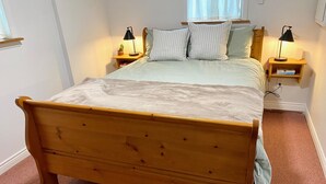 Ein Bett mit Holzkopfschild, zwei Nachttische mit Lampen und ein Fenster mit Vorhängen.
